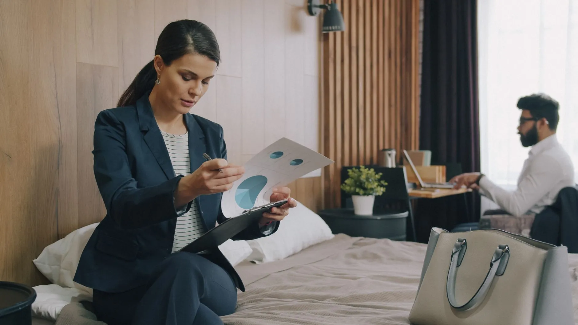 A hotel manager checks report figures at a desk in a hotel room