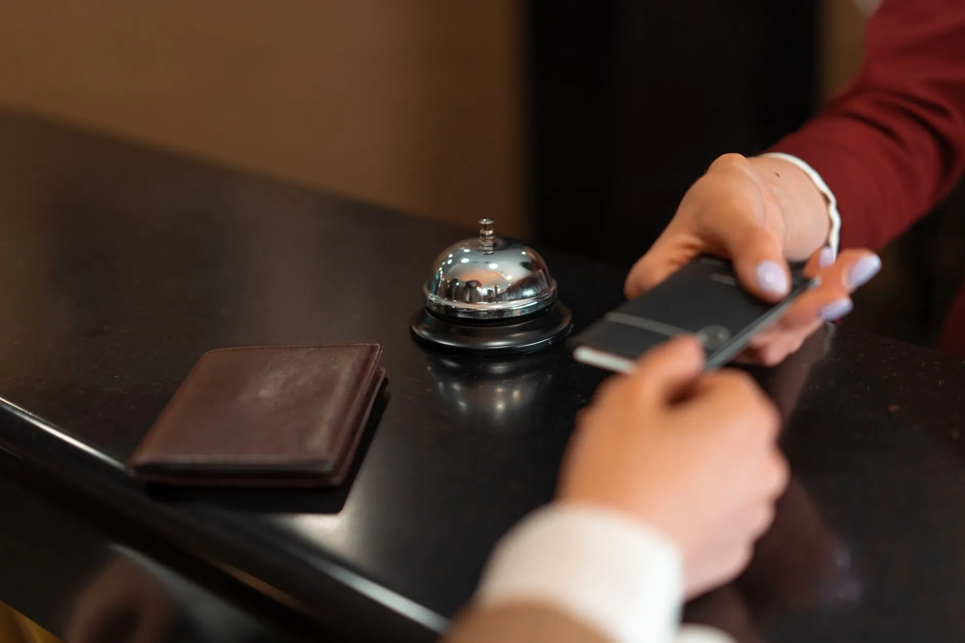 Platba na recepci hotelu: host s telefonem, vedle peněženka – peníze přicházejí při check-inu